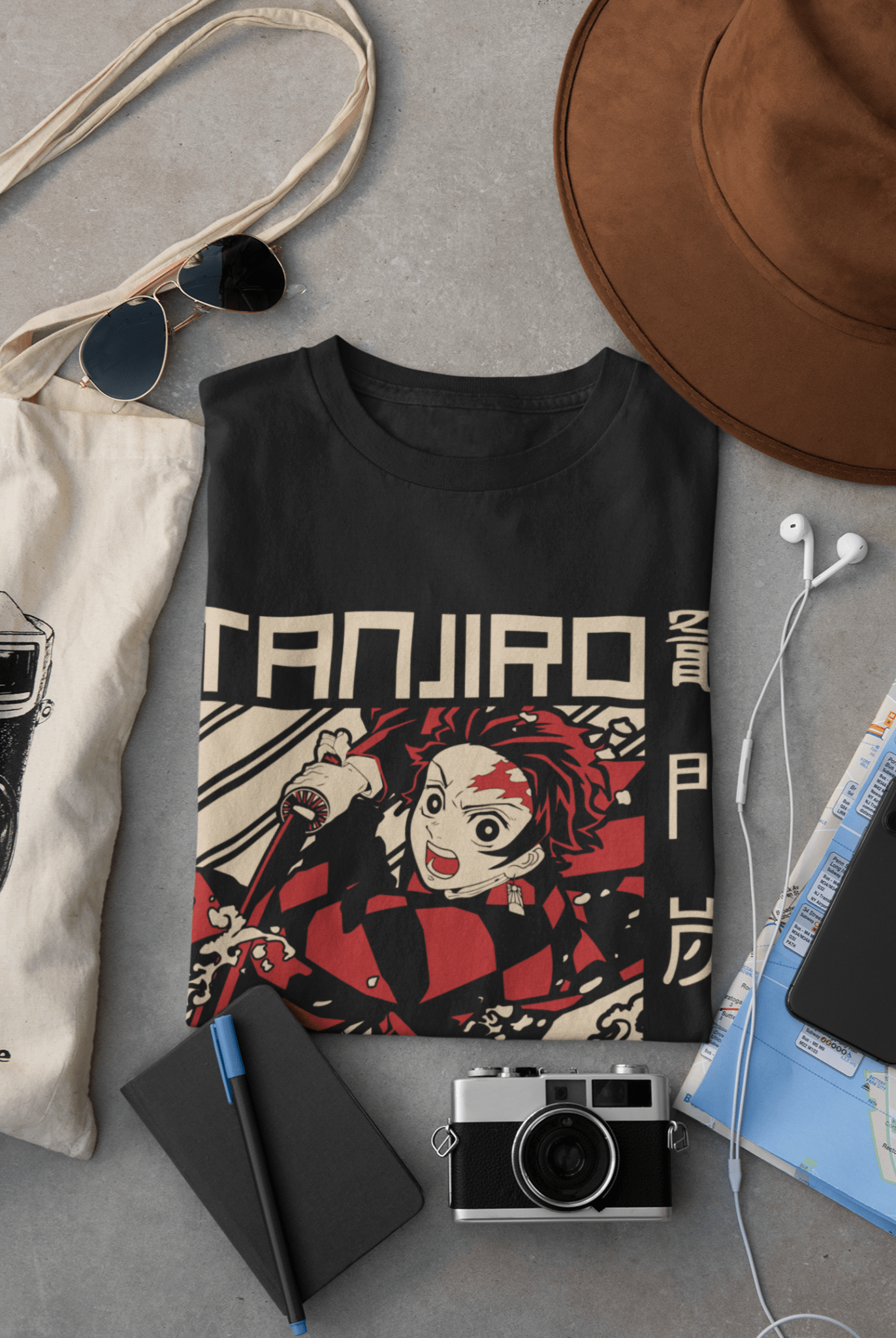 Folded Tanjiro anime t-shirt with travel accessories, camera, hat, sunglasses, and map